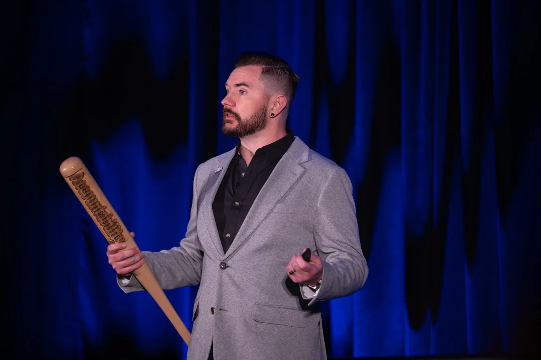 Kyle Christensen on stage holding a wooden bat engraved with the word Accountability